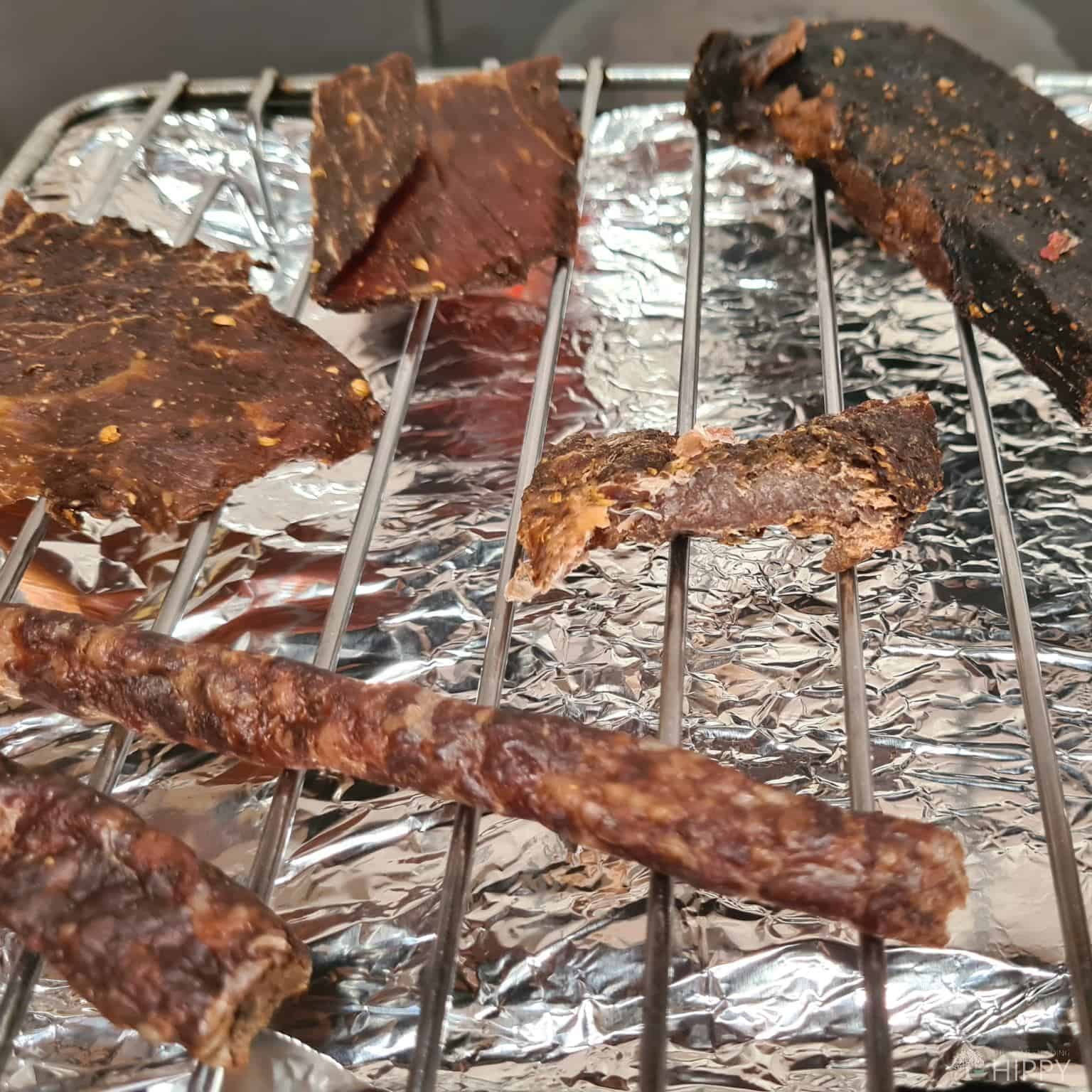 beef jerky and sausages on oven grill above tray