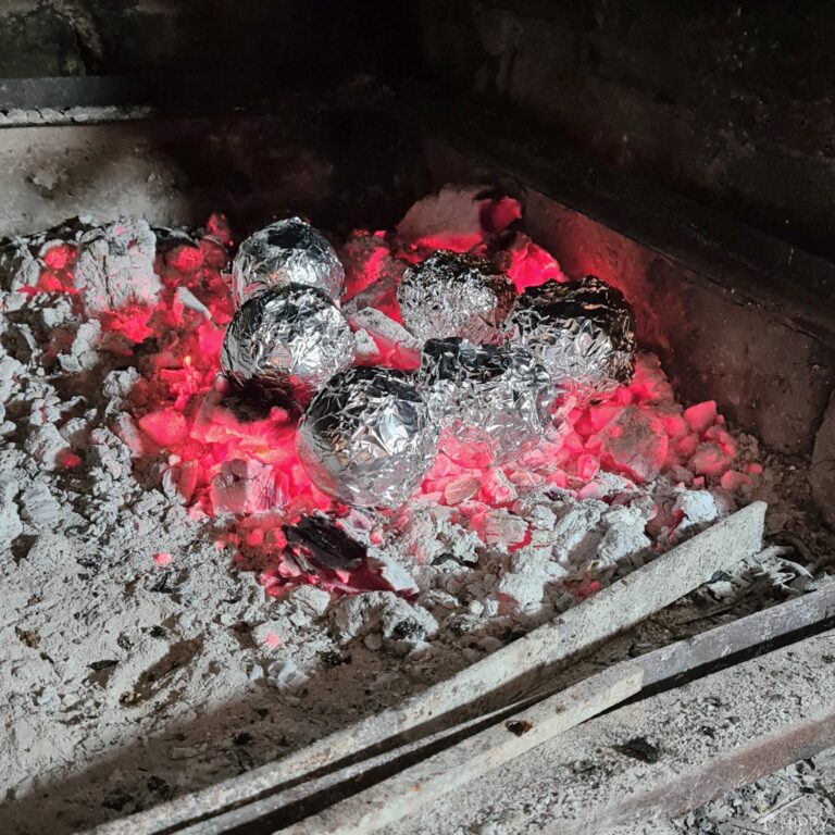 baking potatoes wrapped in aluminium foil on heated coals